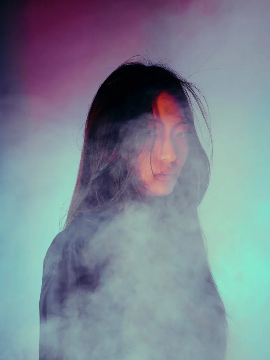 Eine Frau steht im Nebel umgeben von lila und türkisnem Nebel