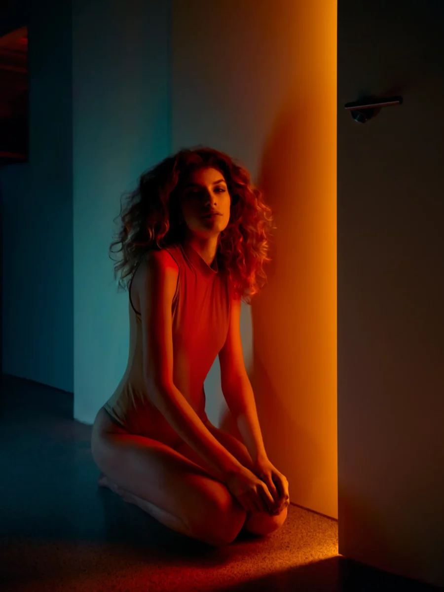 Model sitztend vor offener Tür mit rotem Lichtschein